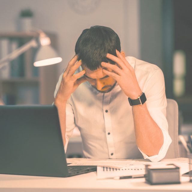 Person sitting at a desk looking overwhelmed in front of a laptop