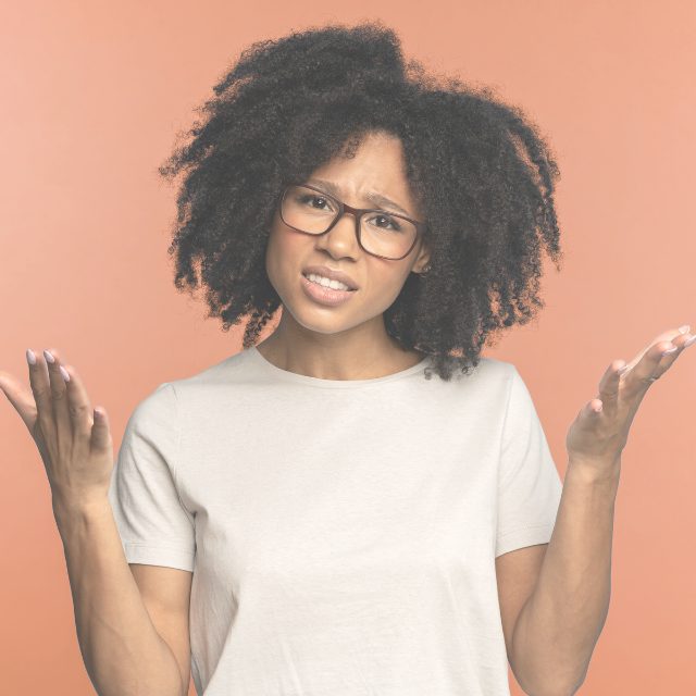 Person shrugging with hands raised against a peach background