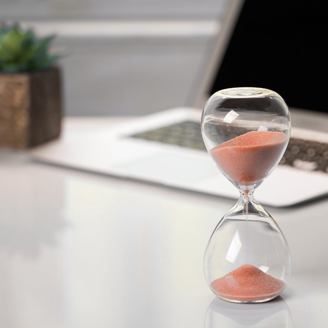 Hourglass on a desk beside a laptop
