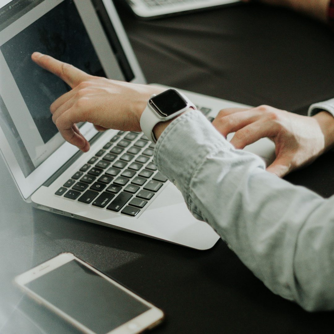 Hand pointing at a laptop screen while checking a smartwatch